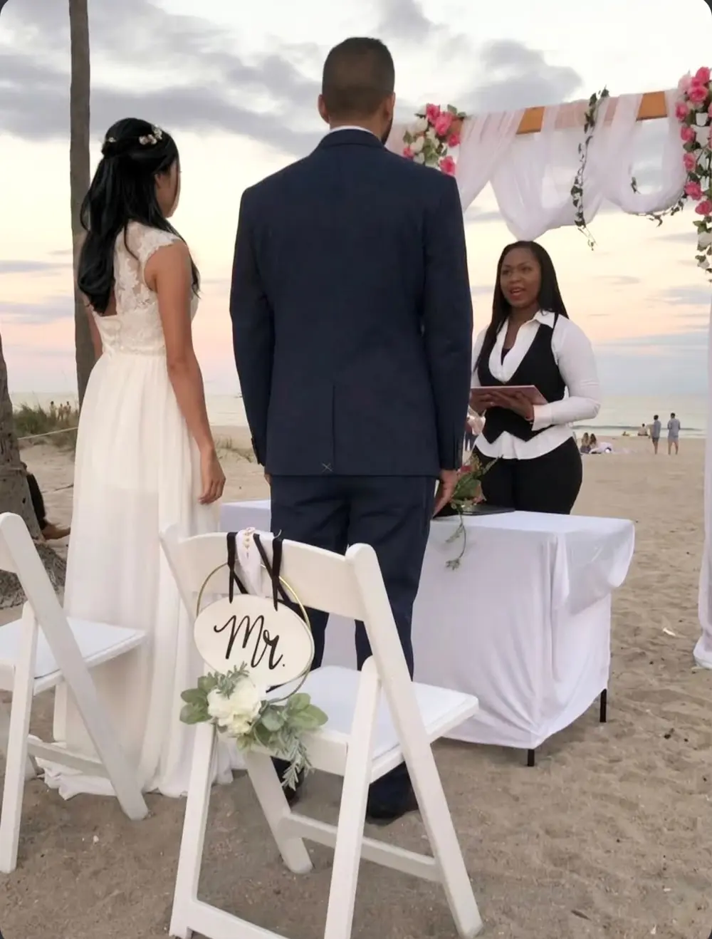 YCONIX officiating a beach wedding ceremony under a floral arch at sunset